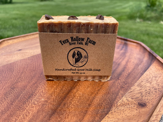 Bar of soap with 'Fern Hollow Farm' label on a wooden surface. The soap is brown with coffee beans on top. 