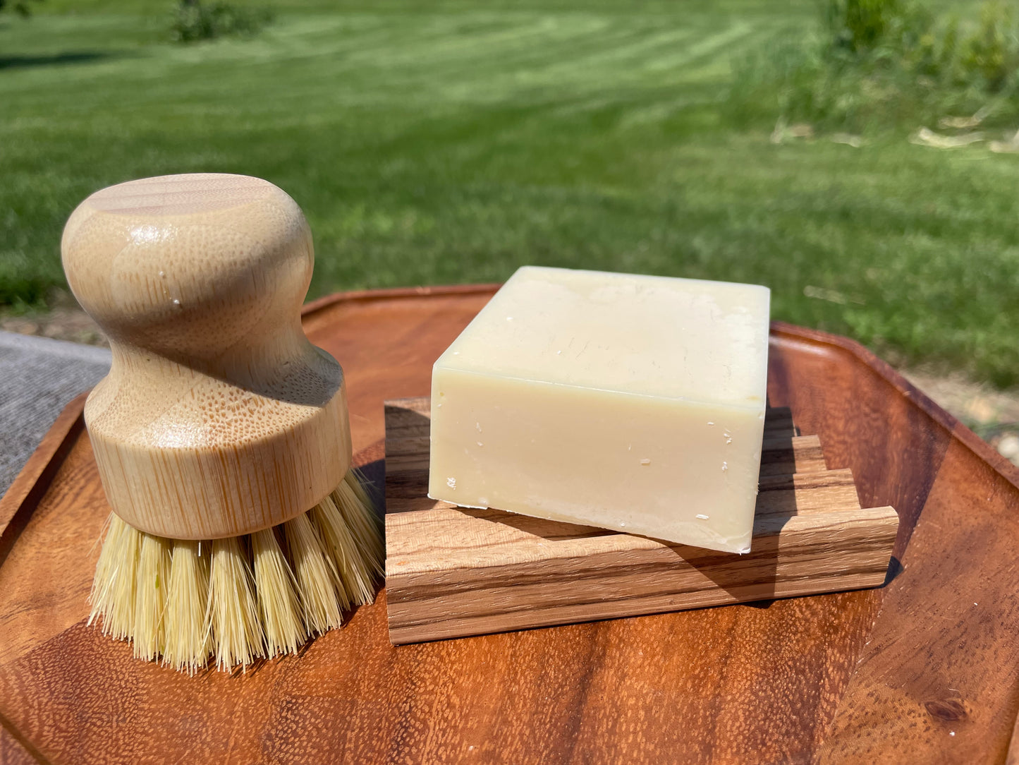 Wooden brush and soap bar on a wooden block with grass in the background