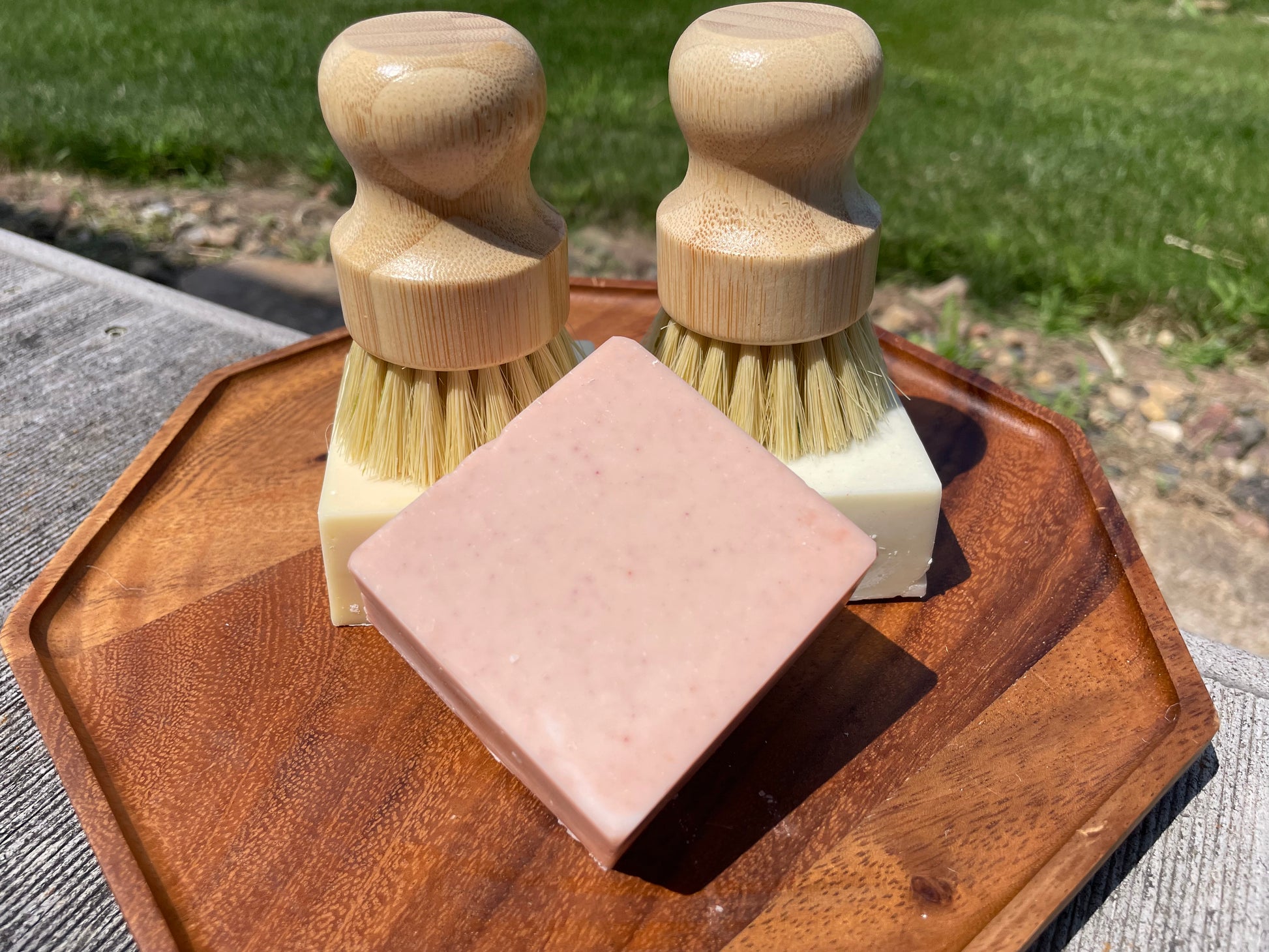 Two wooden brushes sitting on three bars of soap on a wooden tray outdoors.