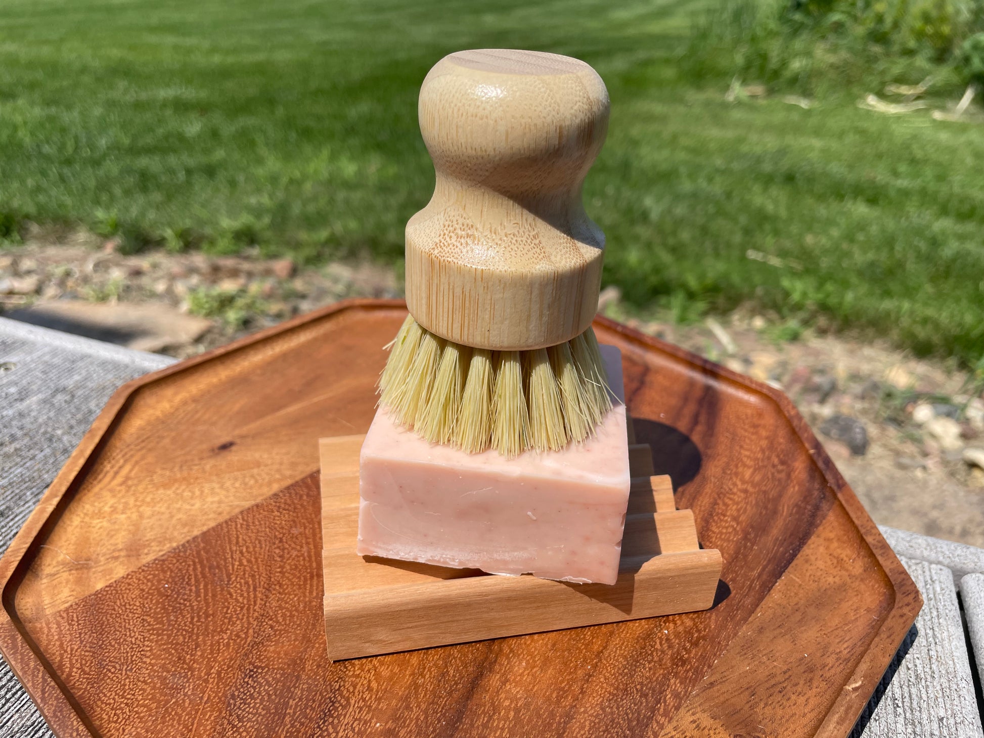 Wooden brush with bristles on a block of pink soap on a wooden soap dish outdoors.