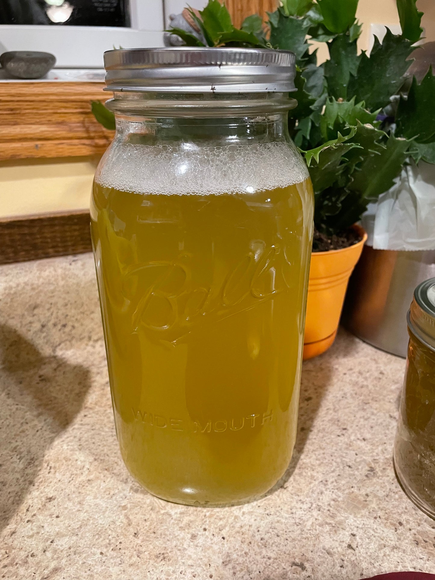 A large half a gallon jar of liquid soap concentrate. The liquid is a dark yellow color. The jar is sitting on a cream countertop. 