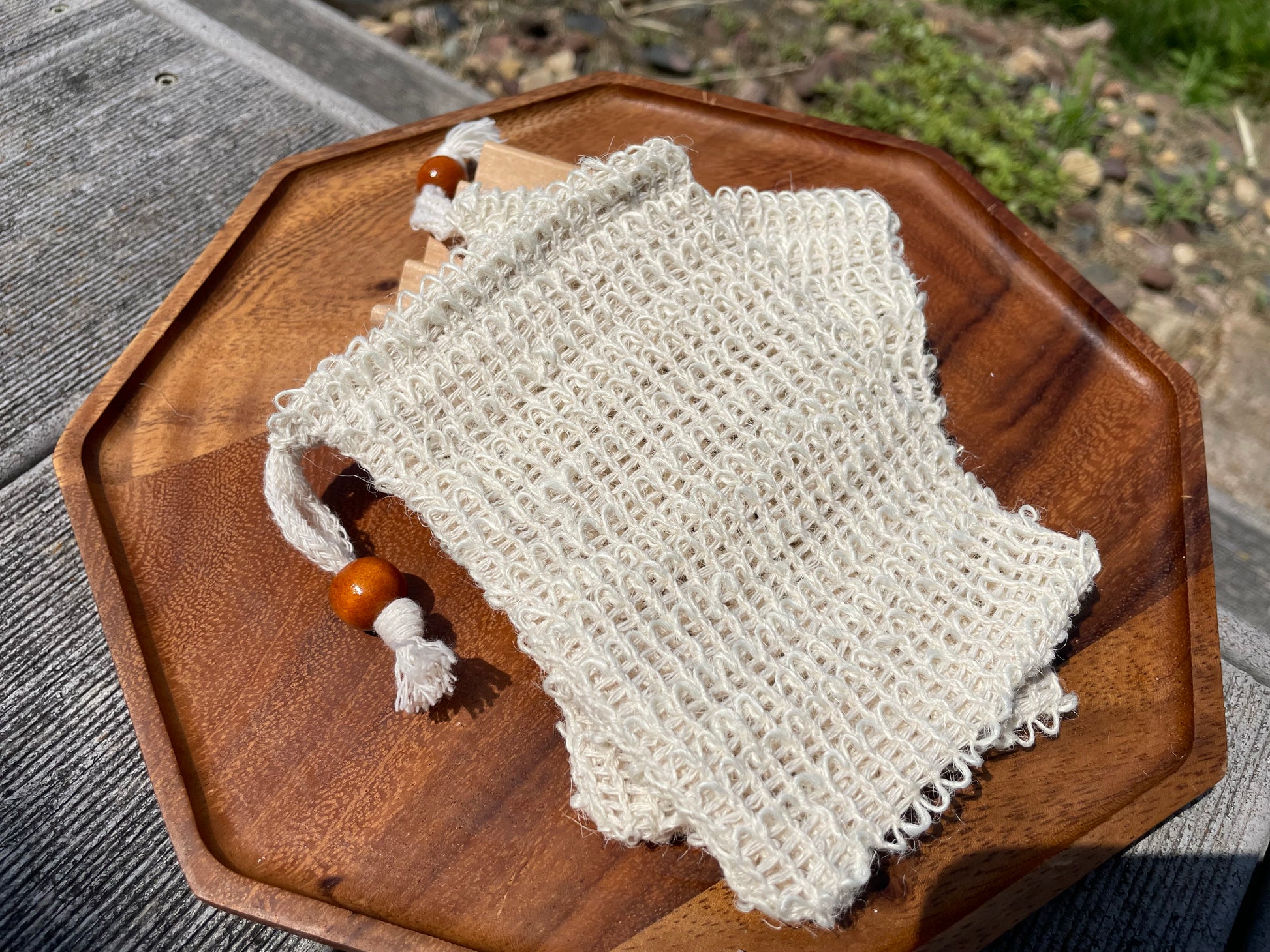 A sisal pouch bag with a wooden bead on the tie on a wooden surface outdoors. 
