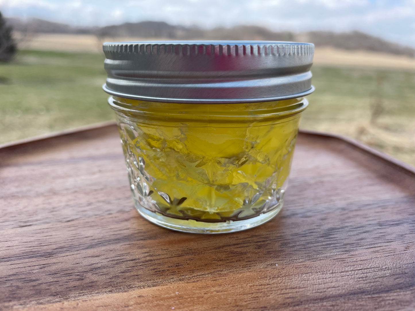 Clear glass mason jar with a yellow gel inside with silver lid. Jar is on a wood surface.