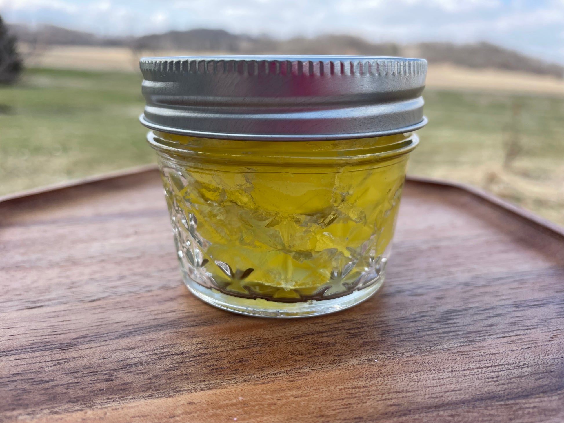 Clear glass mason jar with a yellow gel inside with silver lid. Jar is on a wood surface.