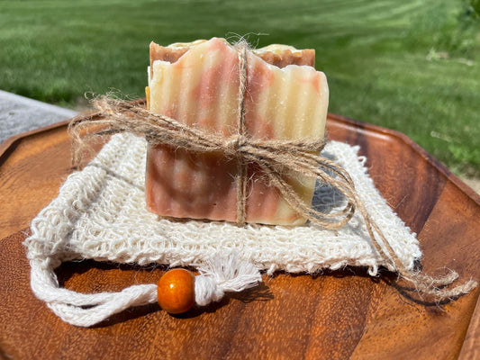 Slices of soap tied with twine on a sisal soap pouch sitting on a wooden surface with a natural background.