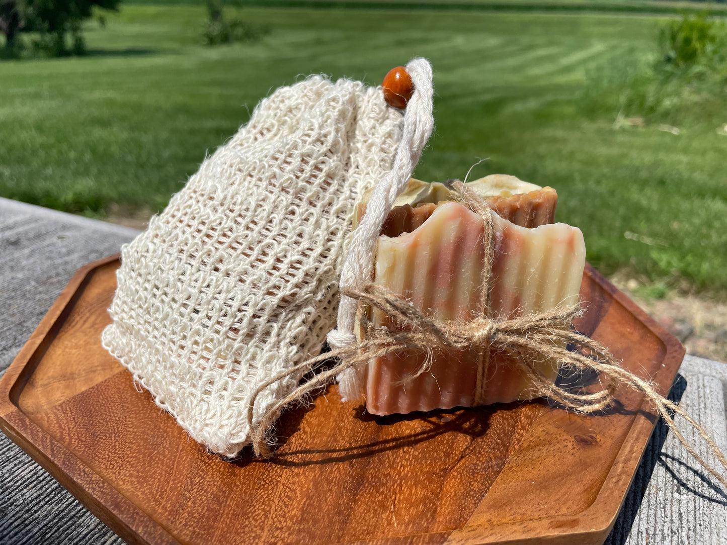 Slices of soap tied with jute string on a wooden board with a textured cloth outdoors.