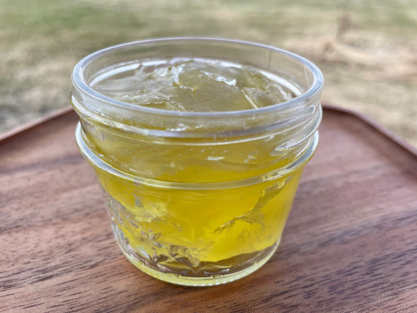 A clear glass jar filled with yellow liquid soap concentrate, placed on a wooden surface.
