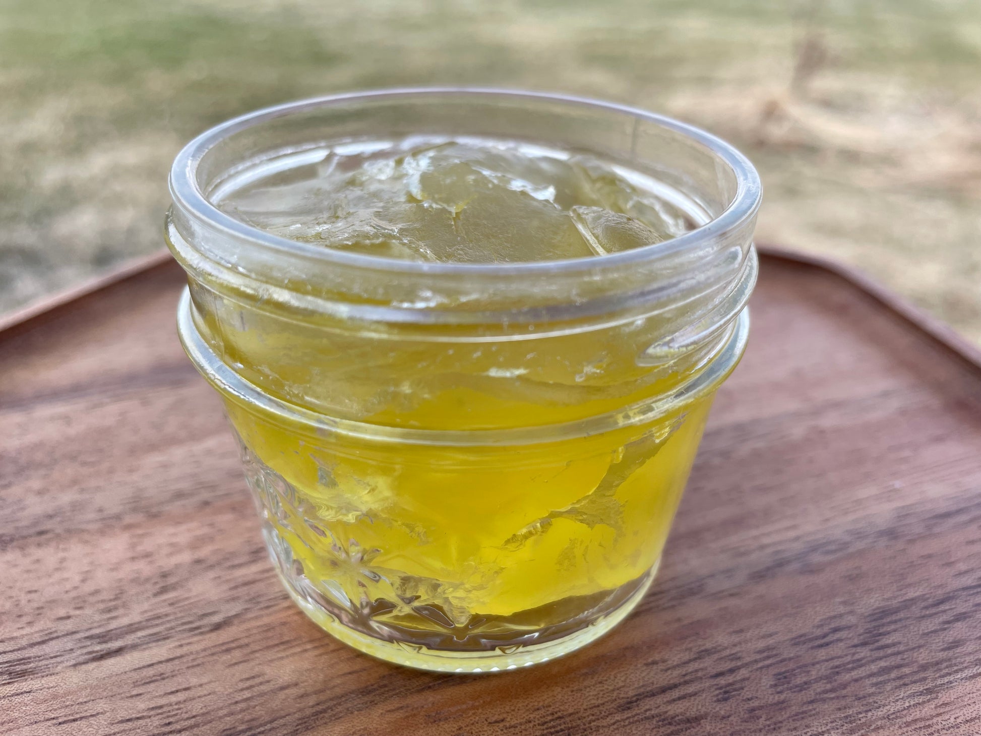 A clear glass jar filled with yellow liquid soap concentrate, placed on a wooden surface.