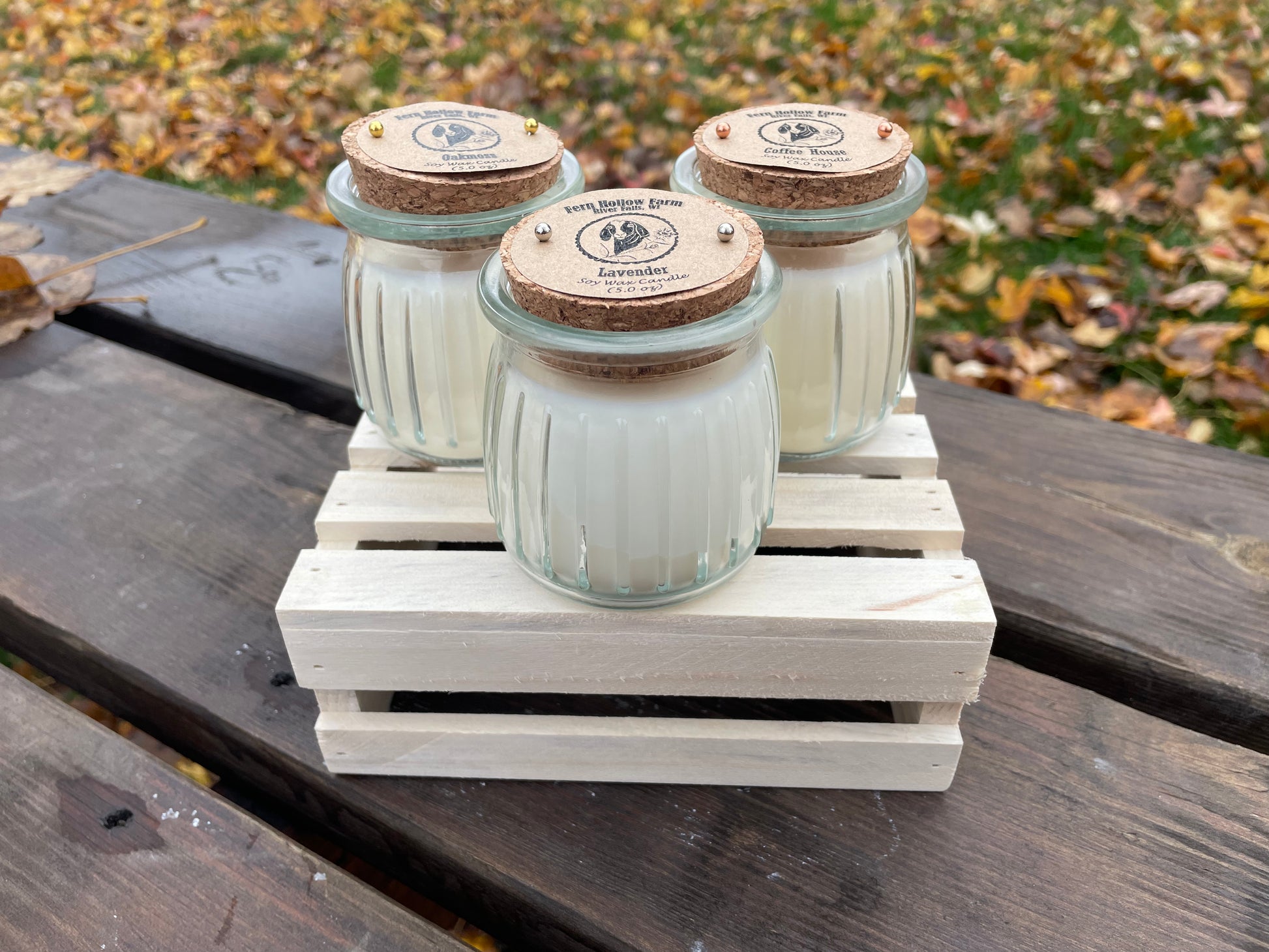 Set of three scented candles in glass jars with cork lids on a wooden crate, featuring lavender and coffee scents.